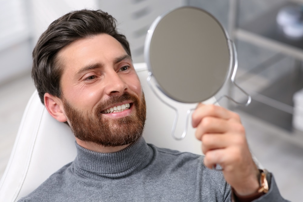 Man,Looking,At,His,New,Dental,Implants,In,Mirror,Indoors